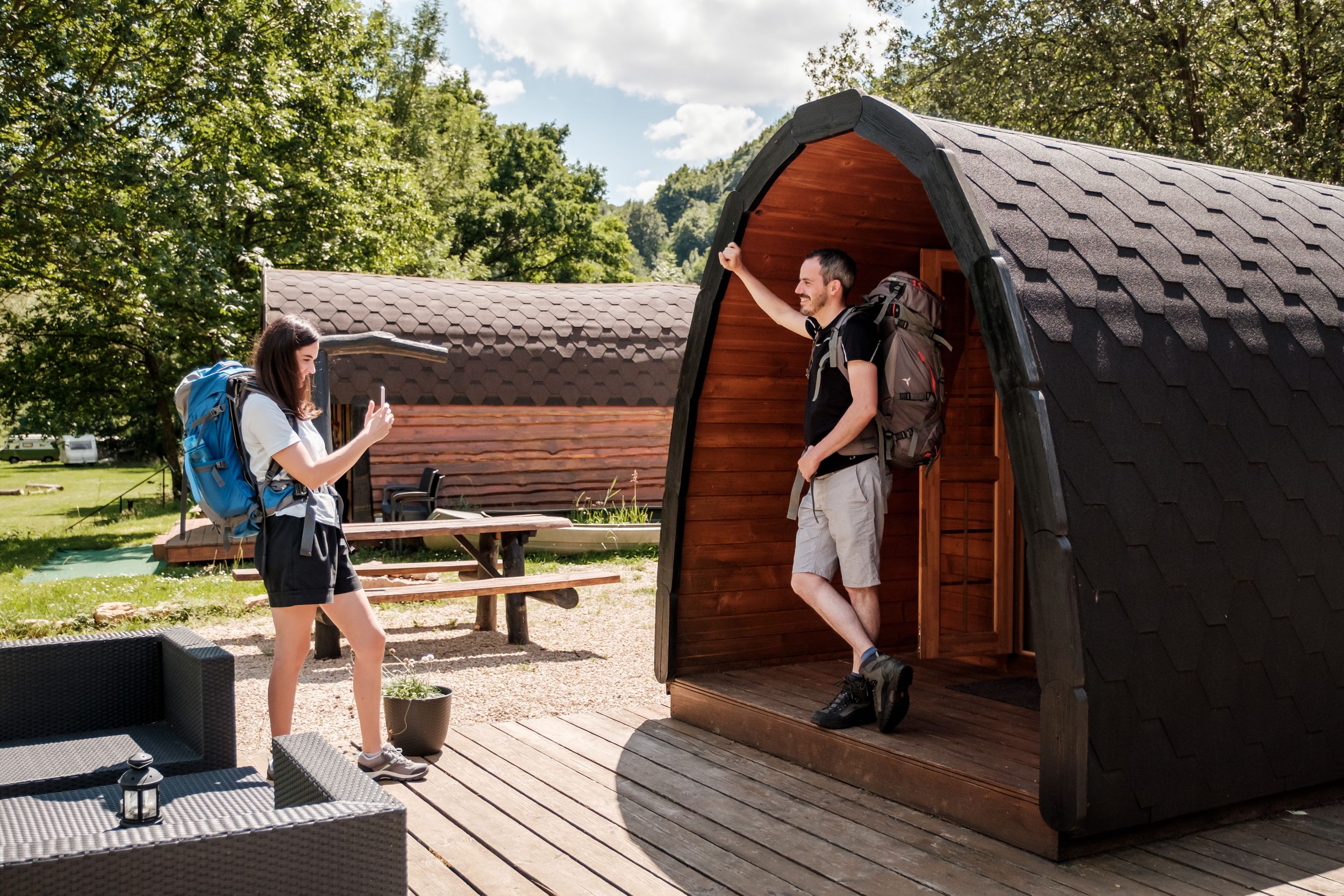 Two people in front of their camping pod, the woman is photographing the man