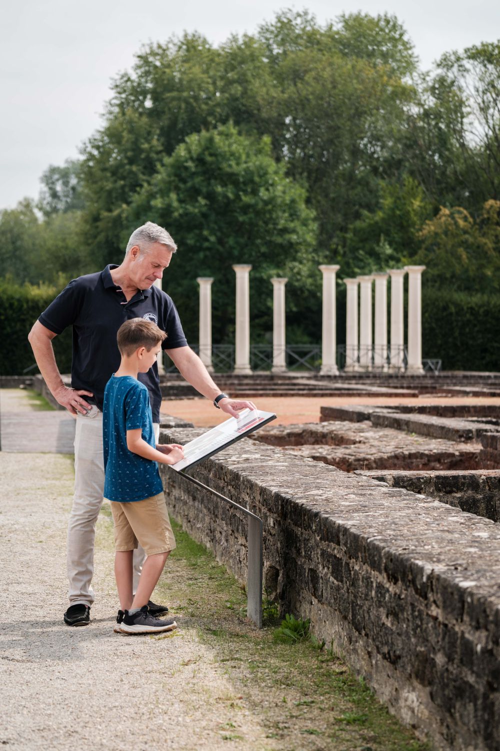 Un père et son fils lisent ensemble le panneau d'information de la villa romaine d'Echternach