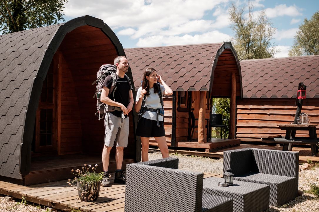 Two people stand in front of their camping pod, ready for a hike.